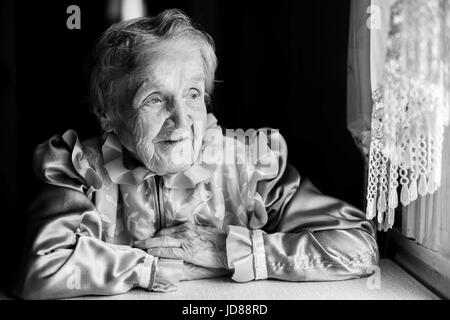 Una donna anziana seduta vicino alla finestra. Nonna slava, un ritratto in bianco e nero. Foto Stock