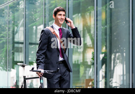 Fiducioso giovane uomo che indossa business suit mentre parlano al telefono cellulare dopo il pendolarismo bici Foto Stock