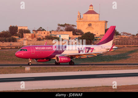 Il viaggio in aereo in Europa. Airbus A320 appartenente alla compagnia aerea bilancio Wizz Air in arrivo a Malta al tramonto, con Ta' Loretu cappella in background Foto Stock