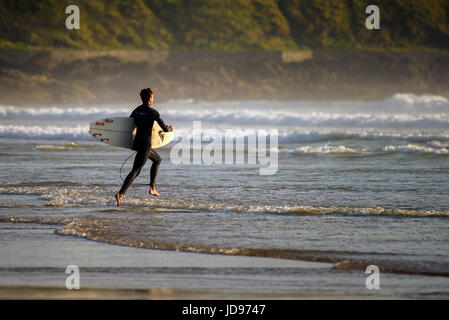 Un surfista che corre in mare a Fistral Beach, Newquay, Cornovaglia. Foto Stock