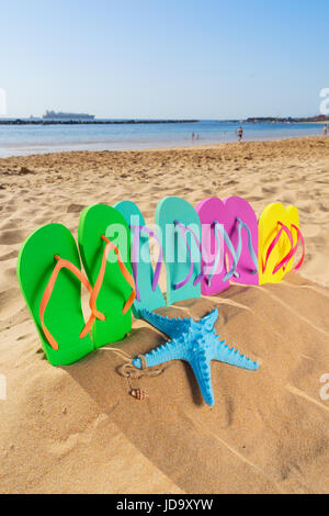 Estate divertente spiaggia - set di colorati sandali di famiglia - verde, blu, rosa e giallo - in sabbia sulla famosa spiaggia di Las Teresitas, Tenerife, Canarie Foto Stock