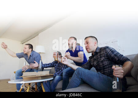 Maschio di amici amanti dello sport guardando vincere una partita di calcio in TV a casa celebra goal vincente rannicchiato sul lettino grida eccitato la condivisione snack Drink Foto Stock