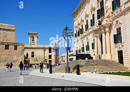 Vista l'Auberge de Castille in Castille Square con turisti che si godono la impostazione e Nostra Signora delle Vittorie chiesa verso la parte posteriore, La Valletta, malto Foto Stock