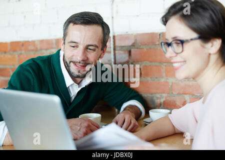 Ritratto di due uomini di affari, uomo maturo e la donna vestita di smart casual lavora con il computer portatile guardando lo schermo e sorridente durante l incontro che ho Foto Stock
