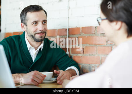 Ritratto di due uomini di affari, uomo maturo e la donna vestita di smart casual guardando ogni altro e sorridente durante la riunione in cafe Foto Stock
