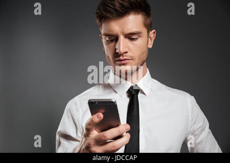 Ritratto di un giovane imprenditore gravi tramite telefono cellulare isolate su uno sfondo grigio Foto Stock