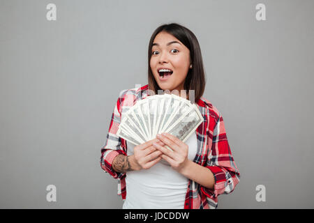 Immagine della giovane donna emotiva azienda denaro oltre il muro grigio. Guardando alla fotocamera. Foto Stock