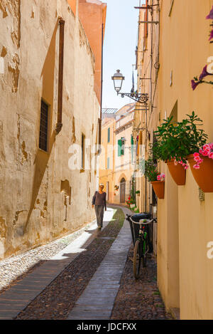 Donna viaggio da solo, vista di una donna che cammina da sola attraverso una stradina nel quartiere della città vecchia di Alghero, Sardegna, Italia. Foto Stock