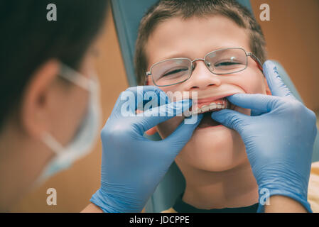 Dentista controllo cellulare apparecchio ortodontico per la correzione dentale per il bambino malato. Close-up. La gente reale. Foto Stock