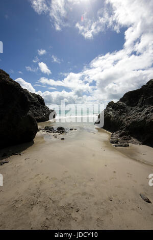 Kynance Cove, in una giornata di sole in Cornovaglia, Inghilterra. Spiaggia di sabbia, mare azzurro e limpido, cielo blu, delimitata da rocce e soffici nuvole. Marea di uscire, impronte Foto Stock