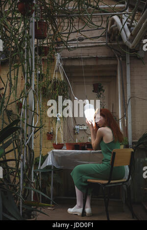 Vista posteriore del giovane ragazza redhead abbraccio lampada in verde mentre è seduto su una sedia e guardando a parte Foto Stock