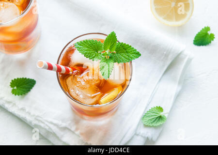 Tè freddo con fettine di limone, menta e cubetti di ghiaccio su sfondo bianco vicino. In casa dissetante bevanda estiva. Foto Stock