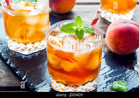 Peach tè freddo. Tè freddo con fette di pesche, menta e cubetti di ghiaccio da vicino. In casa dissetante bevanda estiva. Foto Stock