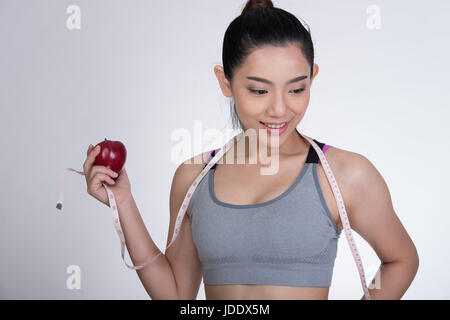 Bella fitness sportivo da donna con nastro di misurazione e mela rossa in piedi contro uno sfondo bianco. dieta, sport e concetto di salute Foto Stock