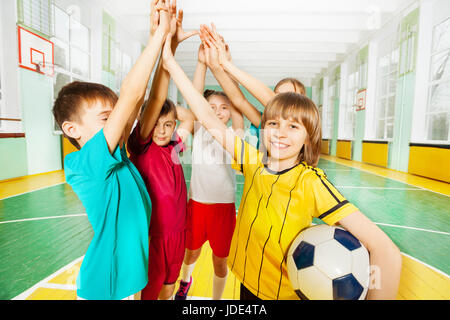 Ritratto di preteen ragazzi e ragazze felici vincitori di calcio, dando alta cinque in sports hall Foto Stock