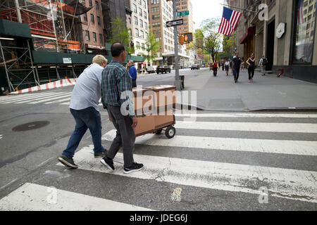 Gli uomini spingendo il carrello consegna attraverso crosswalk nel centro di Midtown New York City USA Foto Stock