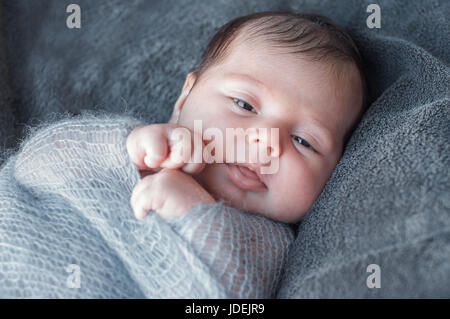Neonato avvolto in maglia calda coperta. Bella closeup ritratto di un neonato che è sveglio e si guarda intorno. Il kid tirata la maniglia di Foto Stock