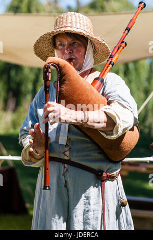 Medieval rievocazione evento, donna matura, vestito come cantore medioevale musicista, in piedi, indossando ampia colmato cappello di paglia riproduzione di cornamuse Foto Stock