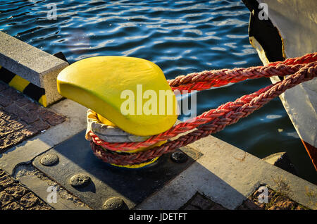 Corda allacciate in un nodo su una bollard. La cima di ormeggio avvolto intorno al gancio sul mare sullo sfondo. Cabestano di metallo nel porto di attracco per yacht e barche Foto Stock