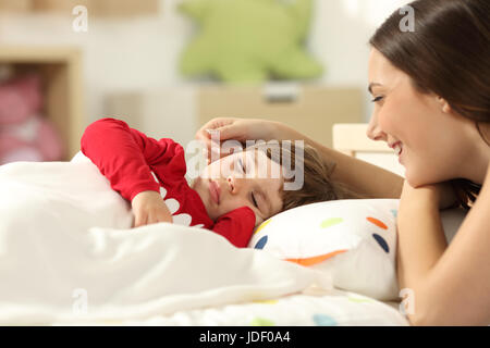 Affettuosa madre guardando la sua ragazza bimbi dormono in un letto nella sua camera da letto a casa Foto Stock