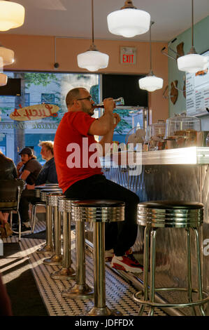 Uomo di bere una soda mentre è seduto a pranzo il contatore in I Love Lucy stile anni '50 diner, Mount Pleasant, Main Street, Vancouver, BC, Canada Foto Stock