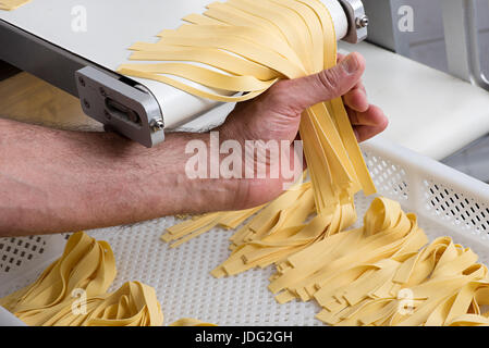 La preparazione preparata di fresco tagliatelle pasta italiana il taglio del rotolo di pasta in nastri con una chef mani è raccolta in fasci su un vassoio Foto Stock