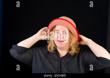 Ritratto di un felice attraente luce europea grassa dai capelli rossi che pongono femmina con un Red Hat - studio shot su sfondo nero Foto Stock
