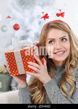 Un attraente giovane donna cercando di capire il dono che ha ricevuto la mattina di Natale, Happy Holiday concept Foto Stock