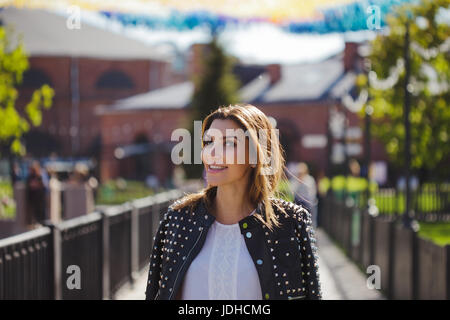 Elegante donna cammina intorno alla città. In una giacca di pelle sulle sue spalle, guarda a voi con un bel sorriso Foto Stock