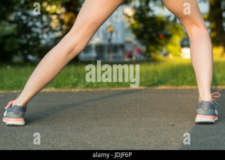 Runner si allunga la gamba su asfalto con scarpe da corsa durante il tramonto da dietro Foto Stock