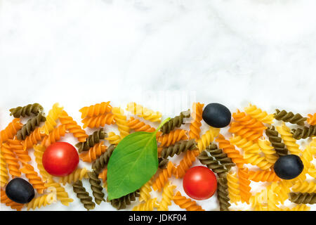 Insalata di pasta ingredienti su marmo bianco con un posto per il testo. Rotini, pomodori ciliegini, di foglie di basilico fresco e olive nere Foto Stock