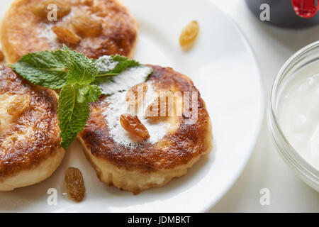 Tre le frittelle su una piastra bianca sul tavolo bianco rivestito con polvere di zucchero, menta, uvetta. basso angolo close up shot. Isolato bianco su bianco Foto Stock