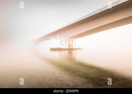 Zeeland ponte (Zeelandbrug) coperta di nebbia durante il sorgere del sole in inverno. Bassa visibilità rendendo il sole che splende attraverso la nebbia la Zeeland bridge è il Foto Stock