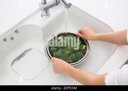 Donna giapponese il lavaggio di broccoli in cucina Foto Stock