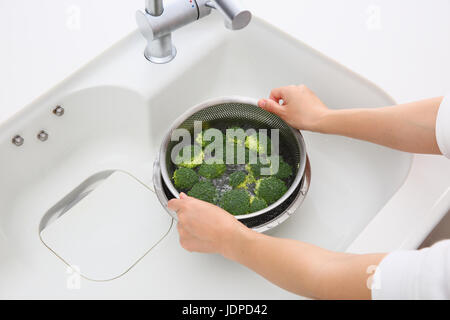 Donna giapponese il lavaggio di broccoli in cucina Foto Stock