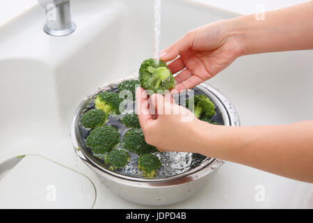 Donna giapponese il lavaggio di broccoli in cucina Foto Stock