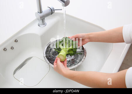 Donna giapponese il lavaggio di broccoli in cucina Foto Stock