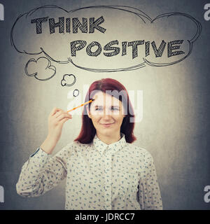 Giovane imprenditrice sorridente, tenendo in mano una matita appuntita per affrontare, disegno pensato bolle sopra la testa. Pensare positivo concetto isolato sul muro grigio backgro Foto Stock