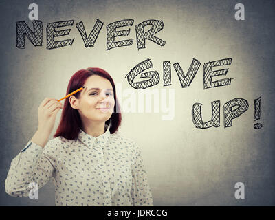Giovani, fiducioso imprenditrice, tenendo in mano una matita appuntita per viso, il disegno di testo sopra la testa. Non mollare mai, pensiero positivo concetto isolato su grigio wa Foto Stock