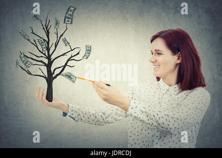 Giovane ragazza sorridente con una matita in mano, disegno disegna un albero magico con dollari che crescono su di esso. Il money tree, il successo commerciale del concetto. Foto Stock
