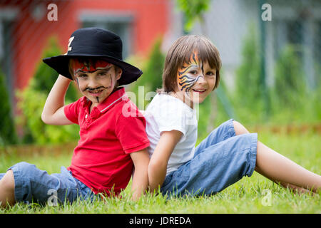 Due figli, fratelli, dipinta come tiger e pirata, giocare insieme in giardino, divertirsi, primavera Foto Stock