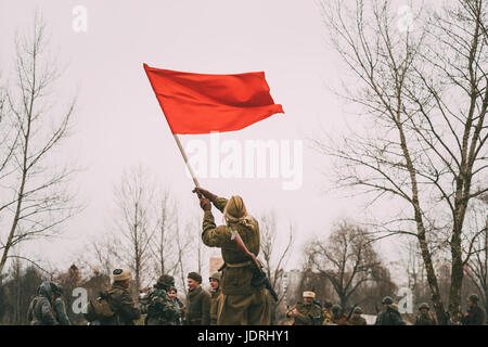 Gomel, Bielorussia - Novembre 26, 2016: Gioiosa ragazza giovane donna Re-enactor vestito come Soviet russo Red Army Soldier of World War II sventola una bandiera rossa in Foto Stock