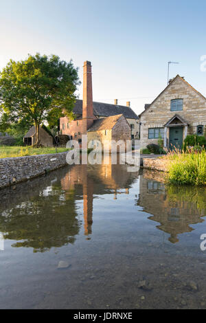 Il vecchio mulino e il fiume occhio con riflessi nella macellazione inferiore nella tarda sera giugno sunshine. Cotswolds, Gloucestershire, Inghilterra Foto Stock