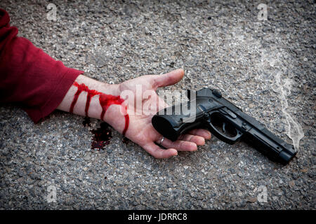 L'uomo con la pistola in mano insanguinata giace morto nell'asfalto vittima di omicidio Foto Stock