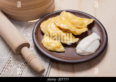 Fresco bollito ucraino caserecci gnocchi di patate con formaggio o ricotta e burro sulla piastra di argilla e con panna acida su sfondo di legno. Varenyky o d Foto Stock