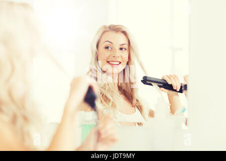 Donna con lo styling ferro facendo i suoi capelli in bagno Foto Stock