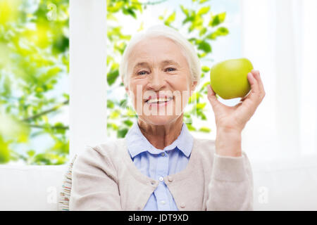 Felice donna senior con mela verde a casa Foto Stock