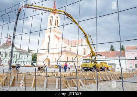 Vista sulla pompa gru per il sollevamento e la colata di cemento in cantiere mediante un filo di recinzione con forma quadratica. Foto Stock