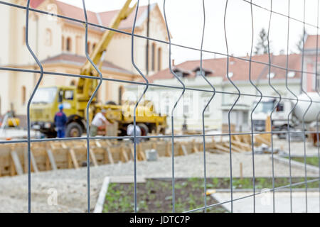 Vista sulla pompa gru per il sollevamento e la colata di cemento in cantiere mediante un filo di recinzione con forma quadratica. Foto Stock