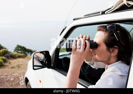 Uomo in auto guardando attraverso il binocolo Foto Stock